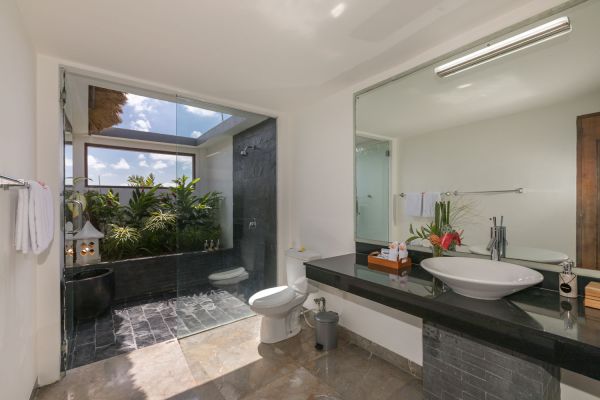 Spacious Balinese-style bathroom with tropical plants, open glass shower, white vanity, and skylight. - Bali Villas