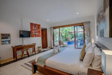 Spacious Balinese villa bedroom with king bed, sliding glass doors to infinity pool, wooden furnishings, and lush garden view.