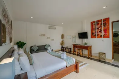 Spacious modern tropical bedroom with wooden bed, green bedding, gray sofa, wall art, and TV in a Bali villa.