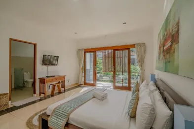 Spacious tropical bedroom with king bed, wooden balcony doors, TV, and en-suite bathroom.