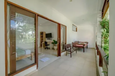 Spacious tropical bedroom suite with open wooden sliding doors to a balcony, wooden furniture, desk, and lush palm views.