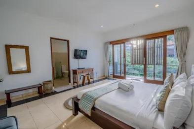 Serene Balinese villa bedroom with king bed, wooden sliding doors to lush garden balcony, TV, desk, and tropical decor.
