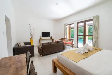 Spacious tropical bedroom with brown leather sofas, wooden bed draped in yellow throw, and sliding doors to a private infinity pool.