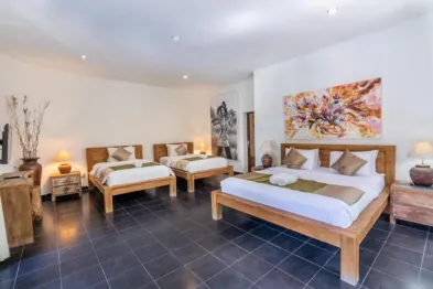 Spacious Balinese bedroom with four wooden twin beds, white linens, abstract wall art, and tropical decor on dark tiled floors.