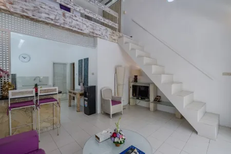 Modern minimalist living room interior with white wooden staircase, bar counter with purple stools, floral coffee table, and neutral decor. - Bali Villas