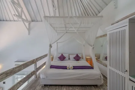Elegant white canopy bed with purple pillows in a airy Balinese-style bedroom.